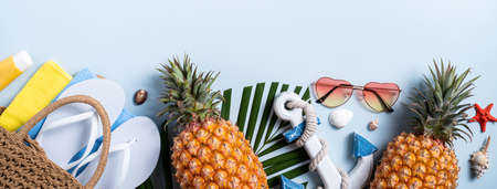 Summer fruit background design concept. Top view of holiday travel beach with shells, hat, pineapple and palm leaves on blue background.の写真素材