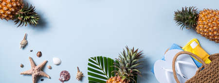 Summer fruit background design concept. Top view of holiday travel beach with shells, hat, pineapple and palm leaves on blue background.の写真素材