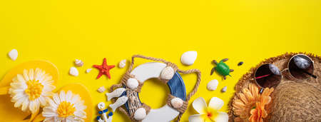 Summer beach design concept. Top view of holiday travel with shells, hat, slipper on yellow...