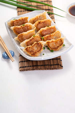 Taiwanese and Japanese Pan-fried gyoza dumpling jiaozi food in a plate with soy sauce on white table background.の写真素材
