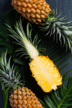 Top view of fresh cut pineapple with tropical leaves on dark blue background.