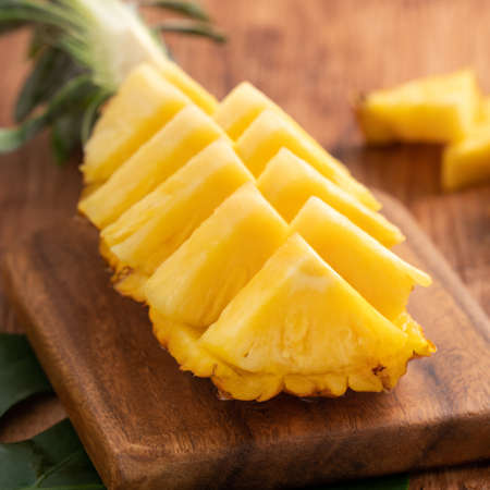 Close up of fresh cut pineapple on a tray over dark wooden table background.の写真素材