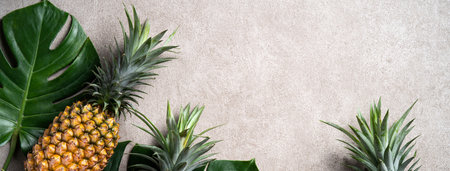 Top view of fresh pineapple with tropical monstera leaves on gray background.