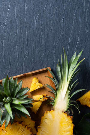 Top view of fresh cut pineapple with tropical leaves on dark blue background.