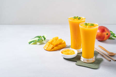 Fresh beautiful delicious mango juice. Close up design concept of smoothie cold drink in glass cup with glass straw on gray table background.の写真素材