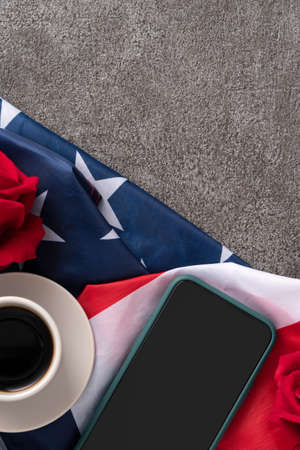 Concept of US Independence day or Memorial day with smart phone and a cupt of coffee. National flag over dark gray table background.の写真素材
