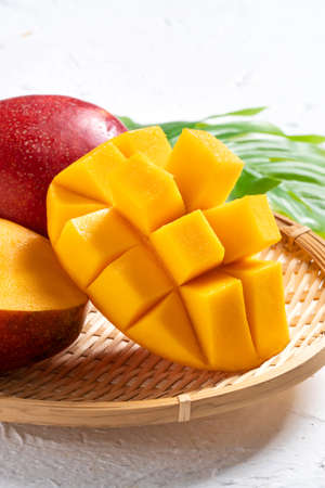 Mango background design concept. Top view of diced fresh mango fruit pattern with leaves on white table.の写真素材