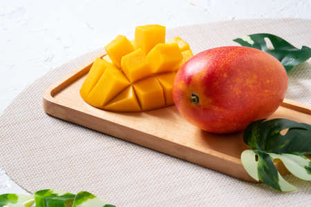 Mango background design concept. Top view of diced fresh mango fruit pattern with leaves on white table.の写真素材