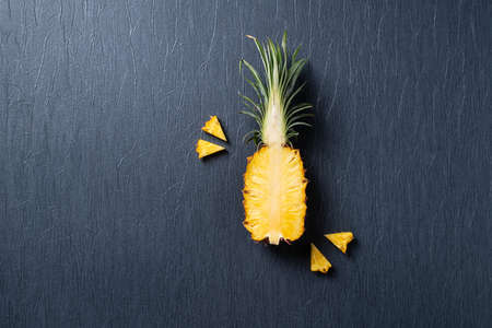 Top view of fresh cut pineapple with tropical leaves on dark blue background.