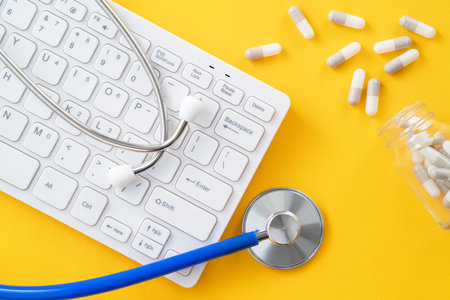 Doctor diagnoses design concept - stethoscope with computer keyboard and capsule pill on yellow background.の写真素材