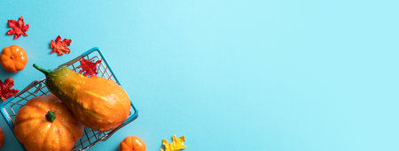 Autumn shopping design concept with shopping cart, maple leaves and pumpkin on blue table background.の写真素材