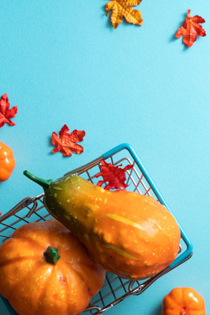 Autumn shopping design concept with shopping cart, maple leaves and pumpkin on blue table background.の写真素材