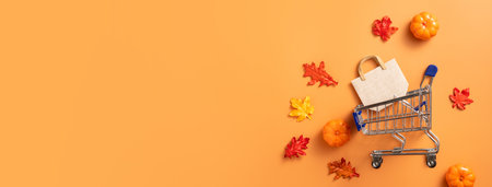 Autumn shopping design concept with shopping cart, maple leaves and pumpkin on orange table...