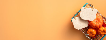 Autumn shopping design concept with shopping cart, maple leaves and pumpkin on orange table background.の写真素材