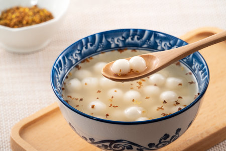 Little white tangyuan (tang yuan, glutinous rice dumpling balls) with sweet osmanthus honey and syrup soup in a bowl on wooden table background.の写真素材