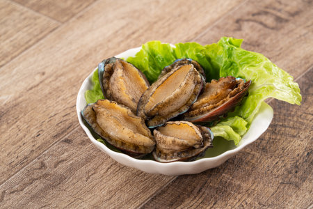 Delicious raw abalone in a plate with lettuce on wooden table background.の写真素材