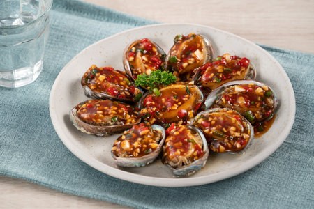 Delicious steamed abalone with spicy tomato sauce, Taiwanese five flavor sauce on wooden table background.の写真素材