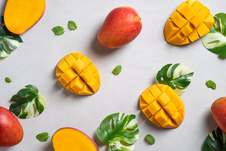 Mango background design concept. Top view of diced fresh mango fruit pattern with leaves on gray table.の写真素材