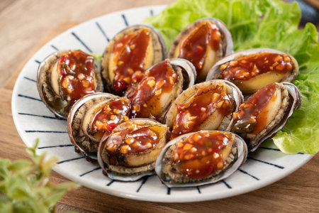 Delicious steamed abalone with spicy tomato sauce, Taiwanese five flavor sauce on wooden table background.の写真素材