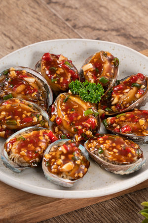 Delicious steamed abalone with spicy tomato sauce, Taiwanese five flavor sauce on wooden table background.の写真素材