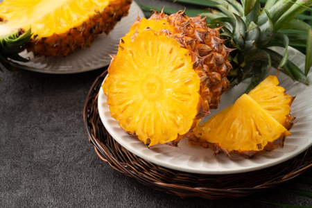 Fresh cut sliced juicy pineapple in a plate over dark gray table background.の写真素材