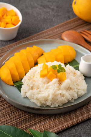 Delicious Thai mango sticky rice with cut fresh mango fruit in a plate on gray table background.の写真素材