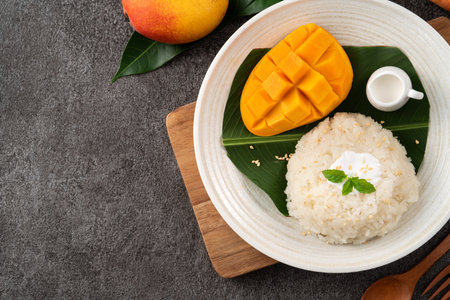 Delicious Thai mango sticky rice with cut fresh mango fruit in a plate on gray table background.の写真素材