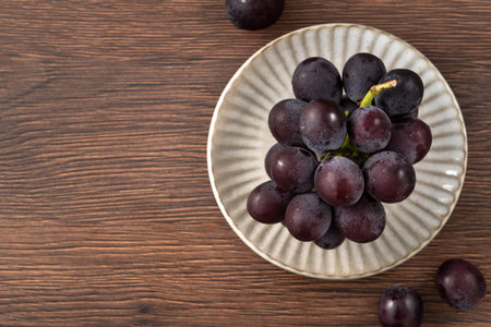 Delicious bunch of purple grapes fruit on a plate on wooden table background.の写真素材