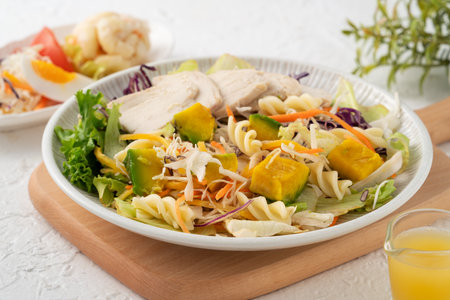 Fresh avocado lettuce salad bowl with sliced chicken meat and rotini on a plate on white table background.の写真素材