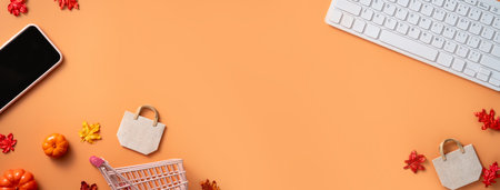 Autumn online shopping design concept with shopping cart, laptop, smart phone and maple leaves on orange table background.の写真素材