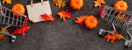 Autumn shopping design concept with shopping cart, maple leaves and pumpkin on black table background.の写真素材