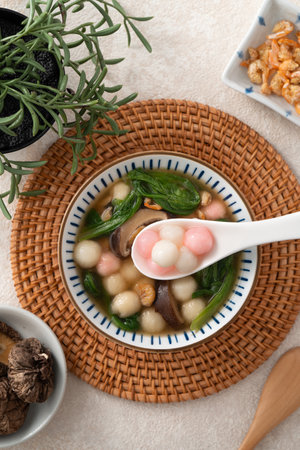 Eating homemade red and white small tangyuan, tang yuan, glutinous rice dumpling balls with savory soup in a bowl on white table background.の写真素材