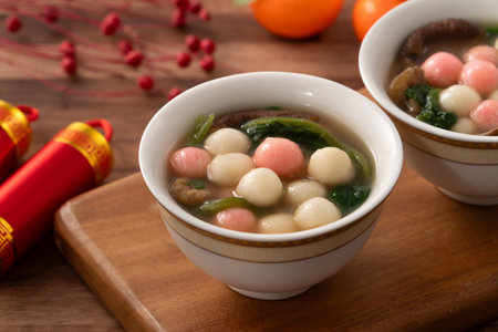 Eating red and white small tangyuan, tang yuan, glutinous rice dumpling balls with savory soup in a bowl on wooden table background for lunar new year festival.の写真素材