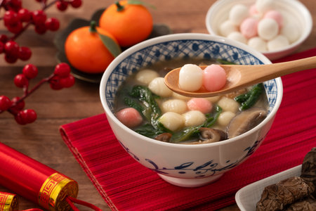 Eating red and white small tangyuan, tang yuan, glutinous rice dumpling balls with savory soup in a bowl on wooden table background for lunar new year festival.の写真素材