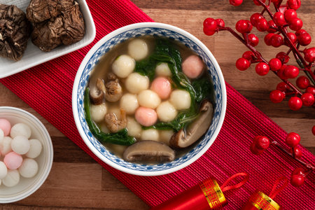 Eating red and white small tangyuan, tang yuan, glutinous rice dumpling balls with savory soup in a bowl on wooden table background for lunar new year festival.の写真素材