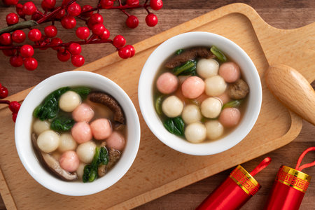 Eating red and white small tangyuan, tang yuan, glutinous rice dumpling balls with savory soup in a bowl on wooden table background for lunar new year festival.の写真素材