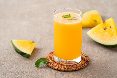 Fresh yellow watermelon juice cold drink in a glass cup with sliced fruit on gray table background.の写真素材