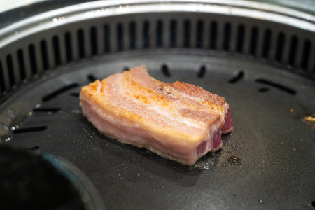 Grilling pork meat on an iron BBQ board in Korean restaurant, fresh delicious food cuisine lifestyle.の写真素材