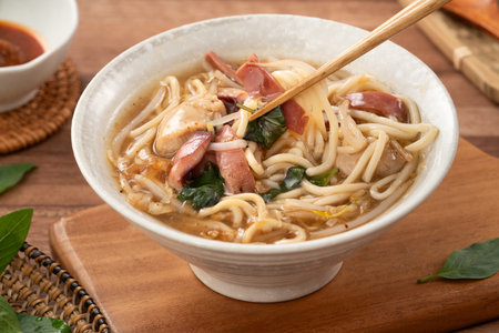 Traditional Taiwanese squid noodle soup with thick broth, served in a ceramic bowl on wooden table.の写真素材
