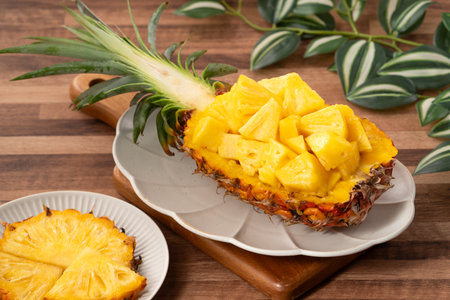 Juicy pineapple chunks arranged in a halved pineapple bowl with tropical leaves in the background.の写真素材