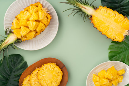 Juicy pineapple chunks arranged in a halved pineapple bowl with tropical leaves in the background.の写真素材