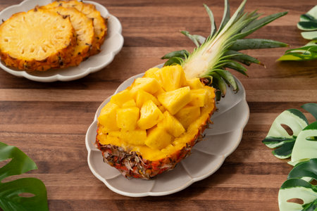 Juicy pineapple chunks arranged in a halved pineapple bowl with tropical leaves in the background.の写真素材