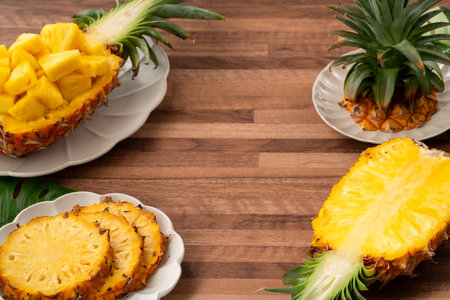 Juicy pineapple chunks arranged in a halved pineapple bowl with tropical leaves in the background.の写真素材