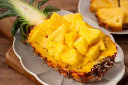 Juicy pineapple chunks arranged in a halved pineapple bowl with tropical leaves in the background.の写真素材