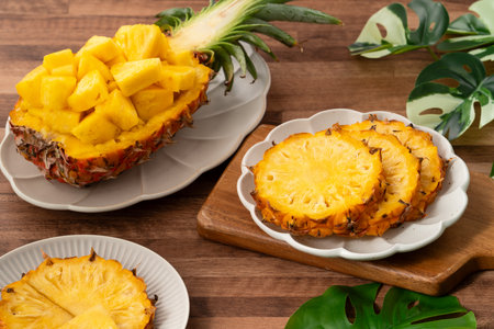 Juicy pineapple chunks arranged in a halved pineapple bowl with tropical leaves in the background.の写真素材