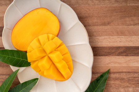 Juicy yellow mango cubes with whole mangoes on a wooden table backgroundの写真素材