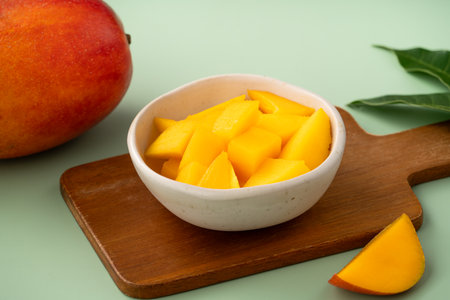 Juicy yellow mango cubes with whole mangoes on a green table background.の写真素材
