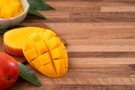 Juicy yellow mango cubes with whole mangoes on a wooden table background.の写真素材