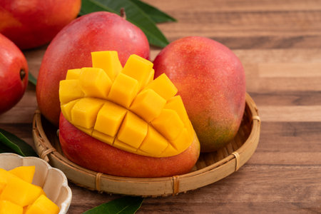 Juicy yellow mango cubes with whole mangoes on a wooden table background.の写真素材