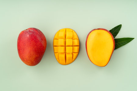 Juicy yellow mango cubes with whole mangoes on a green table backgroundの写真素材